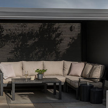 Modern pergola with beige L-shaped sofa and neutral patio styling in a private walled garden.