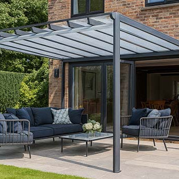 Modern pergola with translucent roof and navy seating set on a stone patio beside a red brick home and green garden.