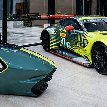 Premium racing simulator with sculpted cockpit and monitor displayed beside an Aston Martin race car in a luxury automotive showroom.