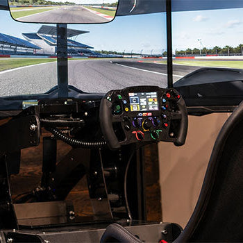 Racing simulator cockpit with triple monitors, motorsport steering wheel and racing seat for an immersive virtual track driving experience.