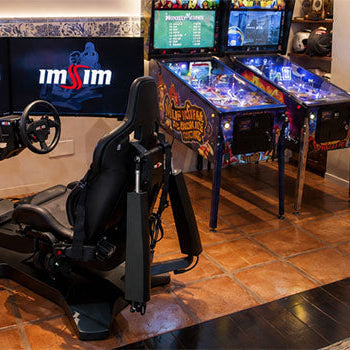 Racing simulator lifestyle setup with dual screens, racing seat and steering wheel in a luxury home games room with arcade machines.