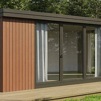 Modern red cedar garden room with sliding glass doors on a wooden deck surrounded by pine trees.