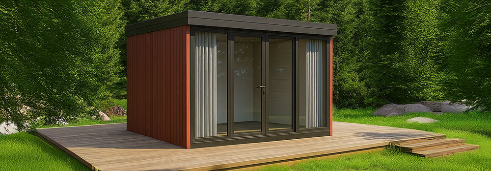 Contemporary red garden room with dark frame glass doors on a wooden deck surrounded by forest greenery under a clear blue sky.