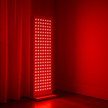 Tall red light therapy panel glowing in a dim minimalist room with wooden flooring and red curtains.