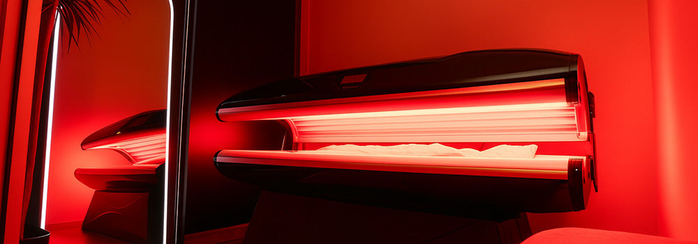 Sleek black red light therapy bed glowing in a luxury room with arched LED mirror and wood floors.