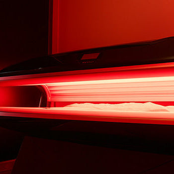 Sleek black red light therapy bed glowing in a luxury room with arched LED mirror and wood floors.