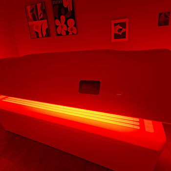 Glowing red light therapy bed in art-filled room with warm wooden floors.