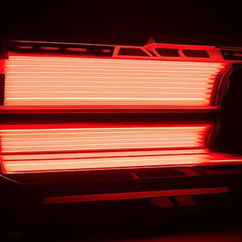 Red light therapy bed glowing in a dark wellness room with open canopy and fluorescent tubes.
