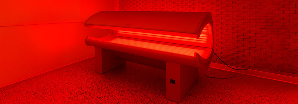 Red light therapy bed glowing in a modern clinical room with speckled flooring and brick accent wall.