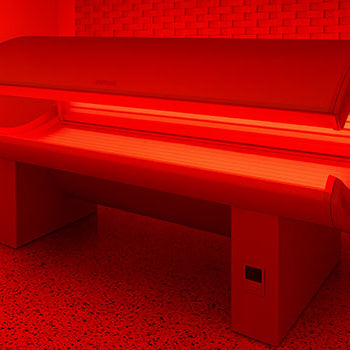 Red light therapy bed glowing in a modern clinical room with speckled flooring and brick accent wall.
