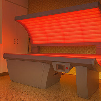 red light therapy bed glowing in a modern interior with white cabinets and patterned wallpaper.