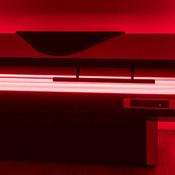 modern red light therapy bed glowing in ambient treatment room with artwork and wood floor.