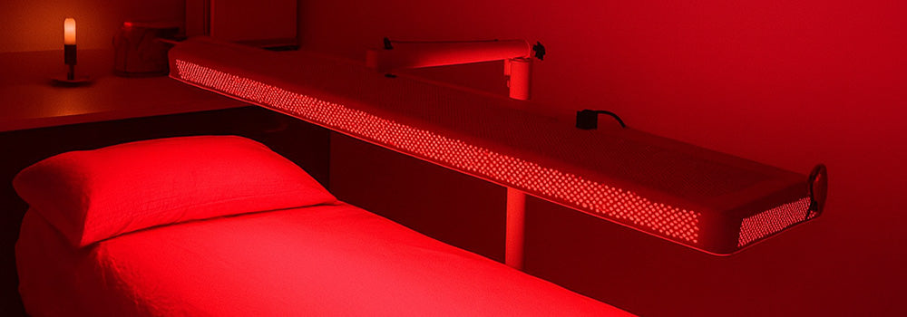 Red light therapy panel above treatment bed in tranquil spa room with candlelight.