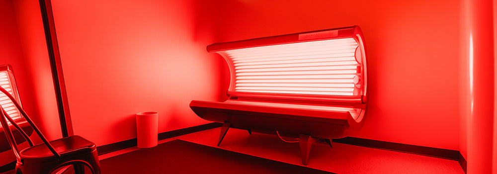 red light therapy bed glowing inside a spa room with red ambient lighting and minimal furnishings.