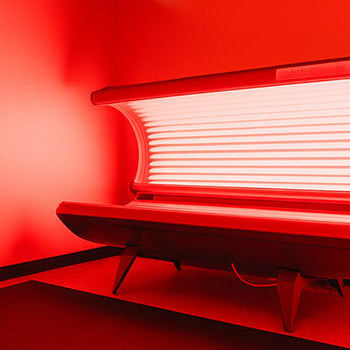 red light therapy bed glowing inside a spa room with red ambient lighting and minimal furnishings.