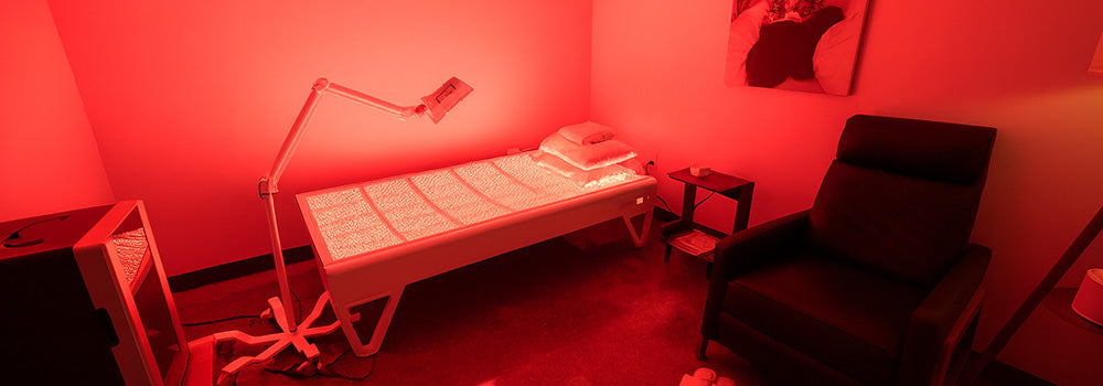 Red light therapy bed in a modern private wellness treatment room with lounge chair and ambient lighting.