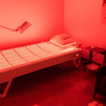 Red light therapy bed in a modern private wellness treatment room with lounge chair and ambient lighting.