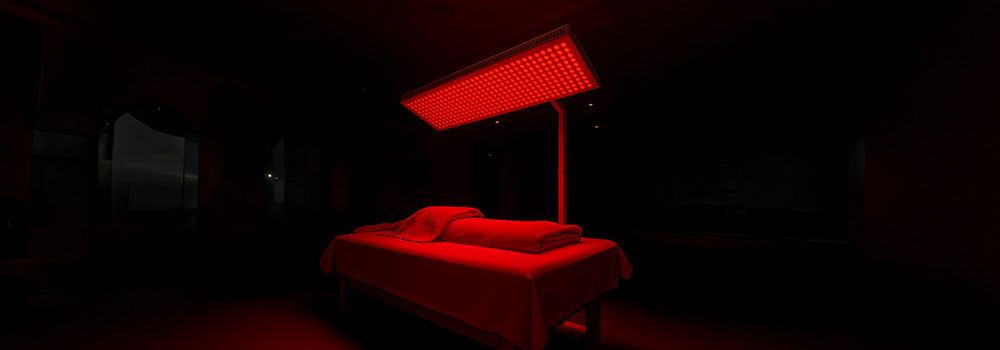 Overhead red light therapy panel illuminating a massage table in a dark wellness room.