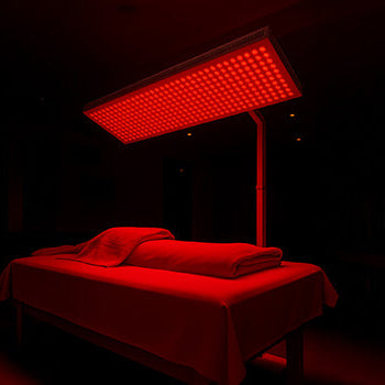 Overhead red light therapy panel illuminating a massage table in a dark wellness room.