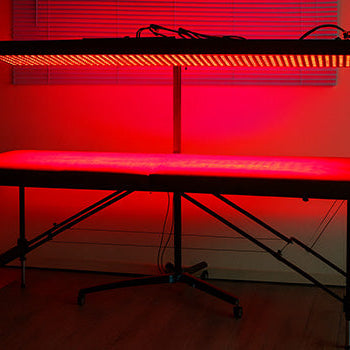 Red light therapy panel glowing above empty massage table in dim room.