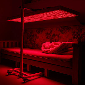 Red light therapy panel glowing above vintage floral sofa with soft blanket.