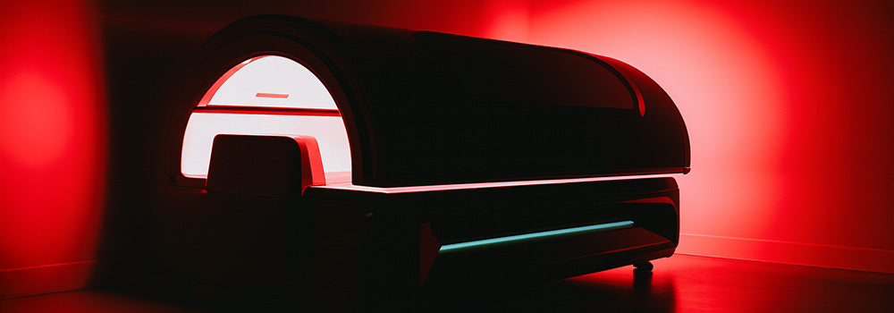 Futuristic red light therapy pod glowing in minimalist dark room with red wall reflections.