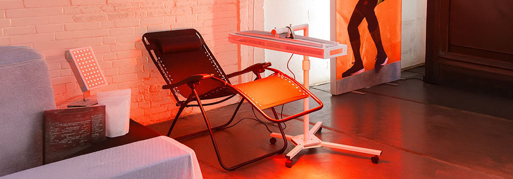 Red light therapy station with recliner and LED panel in an industrial brick space with sports banner.