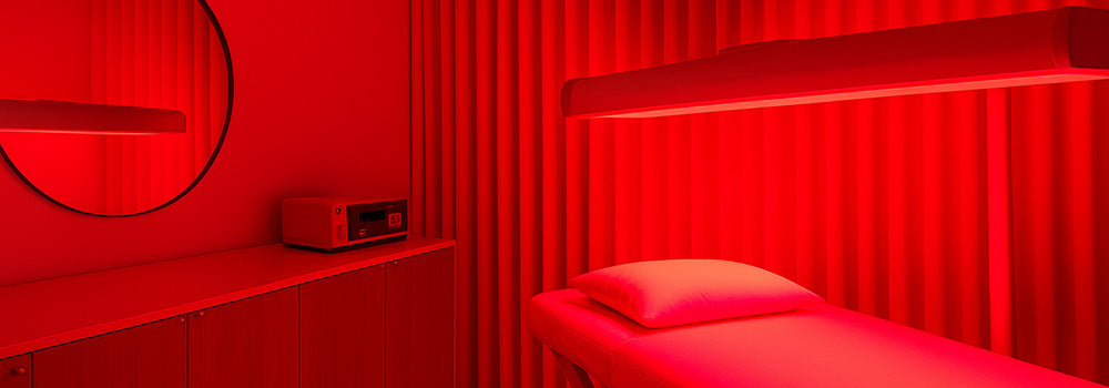 Minimalist red light therapy room with glowing treatment bed, curtain wall, and sideboard under ambient lighting.