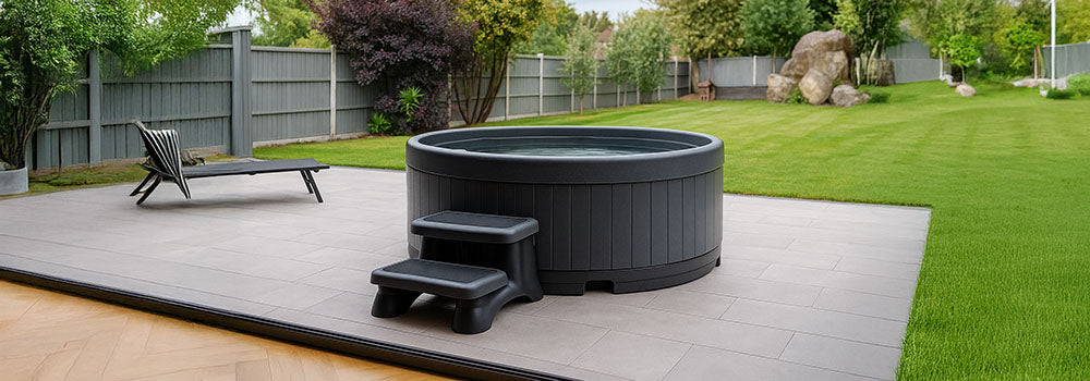 Round rotomoulded hot tub on tiled patio with steps in landscaped backyard.