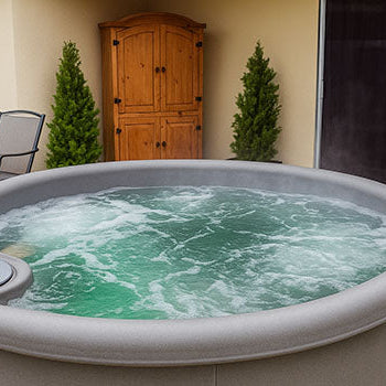 Round rotomoulded hot tub with bubbling green water on a patio with garden plants.