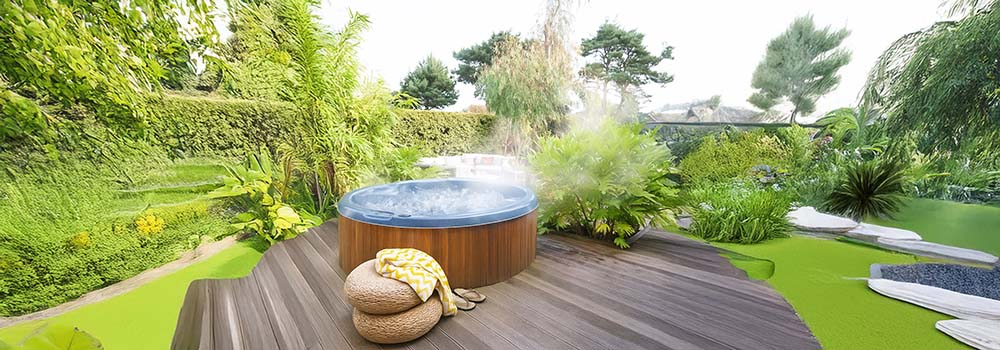 Steaming round hot tub on wooden deck surrounded by tropical garden.