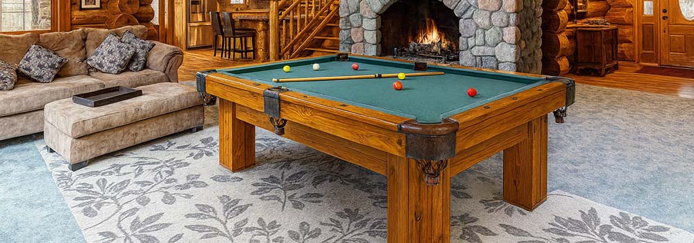 rustic log cabin interior with a wooden pool table and stone fireplace under a wagon wheel chandelier.