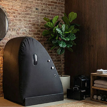 White soft hyperbaric oxygen chamber in a clean, modern wellness room with light wood floors and minimalist decor.