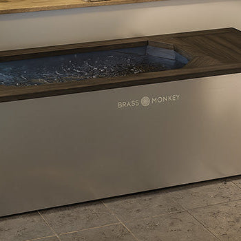 Stainless steel ice bath with dark wood top in modern indoor spa setting with towels and plants.