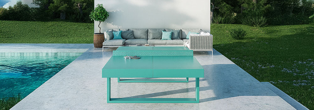 Turquoise outdoor table tennis table on a marble patio beside a pool with modern grey seating and forest backdrop.