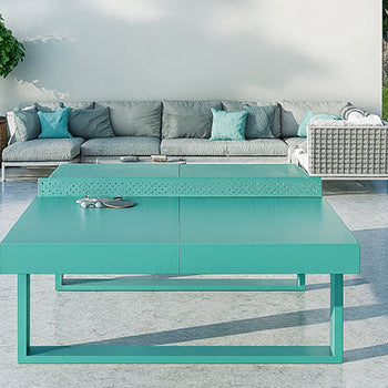 Turquoise outdoor table tennis table on a marble patio beside a pool with modern grey seating and forest backdrop.