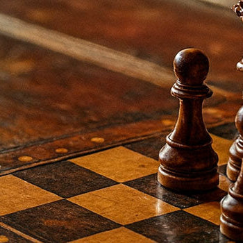 Vintage wooden chess set on rustic table with brass lamp and velvet drapes in warm, classic interior.