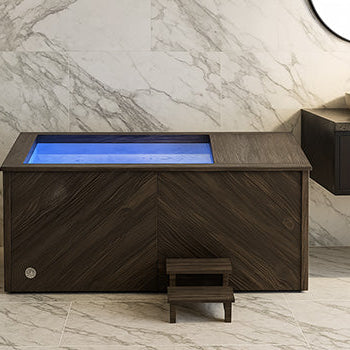 Dark wood ice bath with blue LED lighting in a luxury marble bathroom with stone sink.