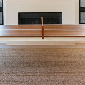 Modern wooden table tennis table with white frame in a bright living room with black-trim windows and fireplace.