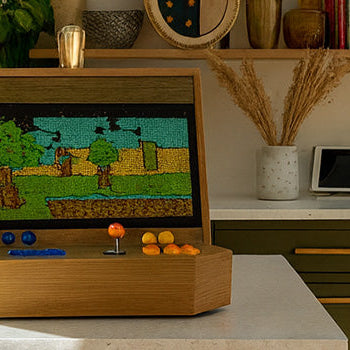 wooden arcade machine with blue and orange controls on a kitchen island in a warm, sunlit modern home interior.
