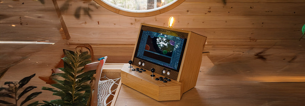 tabletop arcade machine with black joysticks and space game display in a cozy wood-paneled cabin by a round window.