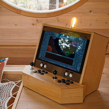 tabletop arcade machine with black joysticks and space game display in a cozy wood-paneled cabin by a round window.