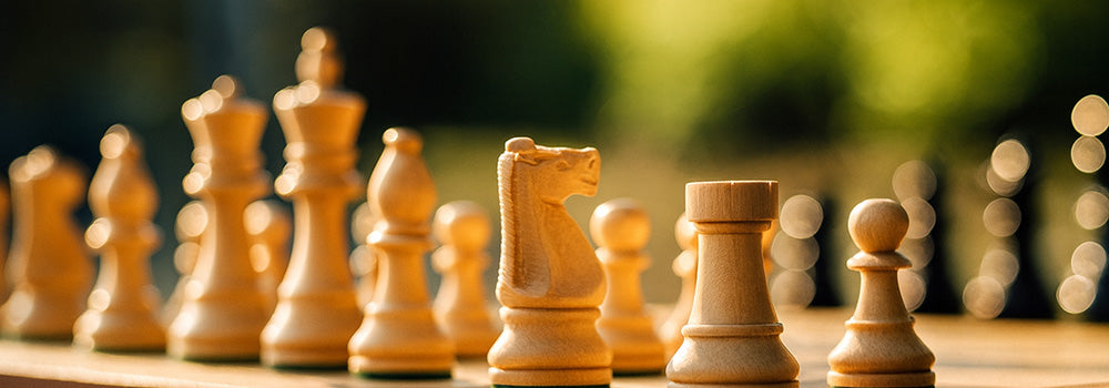 Luxury wooden chess set in golden hour sunlight on outdoor table with blurred garden background.