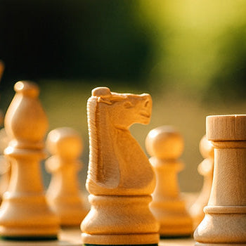 Luxury wooden chess set in golden hour sunlight on outdoor table with blurred garden background.