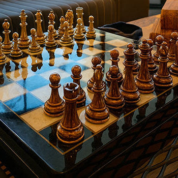 Luxury wooden and gold chess set on glossy marble board in modern lounge with elephant sculpture.