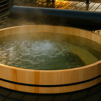 Steaming wooden hot tub on a wet deck at sunset with rolled-up cover.