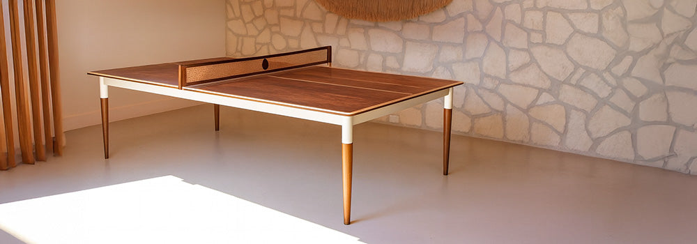 Elegant wooden table tennis table in a bright rustic room with stone wall, rattan pendant light, and fringe wall art.