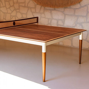 Elegant wooden table tennis table in a bright rustic room with stone wall, rattan pendant light, and fringe wall art.