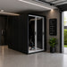 Altitude Centre MetraFit 3000 POD in black with white-framed sliding glass doors and exercise bike inside, installed in a smart home garage alongside a dark saloon car.