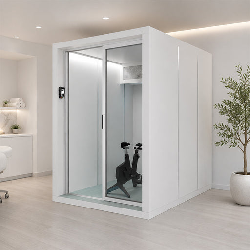 Altitude Centre MetraFit 3000 POD in white with aluminium-framed sliding glass doors, exercise bike inside, installed in a spa treatment room with marble counter and treatment bed.